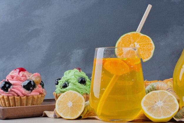 A glass of lemonade and creamy cupcakes on table.