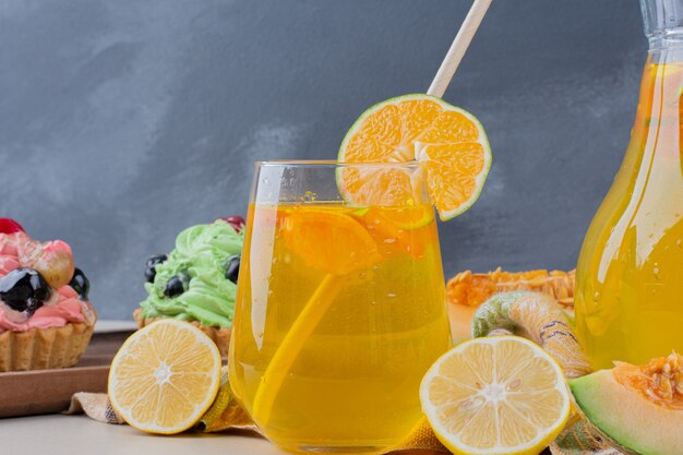 A glass of lemonade and creamy cupcakes on table.