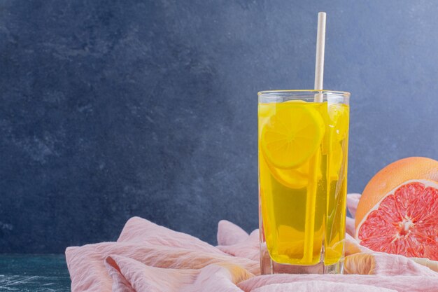 A glass of lemonade with lemon slices and grapefruits on marble surface.