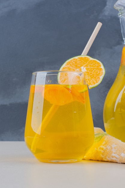 A glass of lemonade with lemon slices on white table.