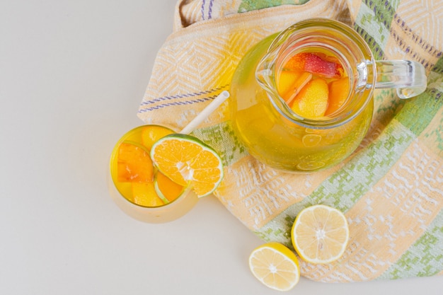 Glass of lemonades with lemon slices on white surface.