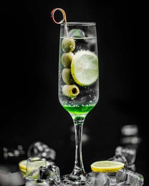 A glass of martini with olives and lemon slice.