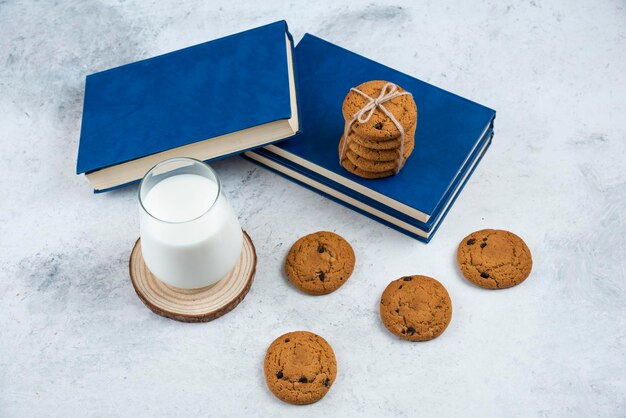 Foto gratuita bicchiere di latte, biscotti al cioccolato e libro sulla superficie di marmo.