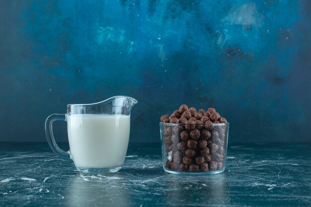 파란색 배경에 유리 그릇에 옥수수 공 옆에 우유 한 잔. 고품질 사진