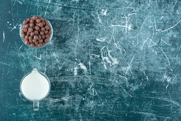 Un bicchiere di latte accanto a palline di mais in una ciotola di vetro, sul tavolo blu.