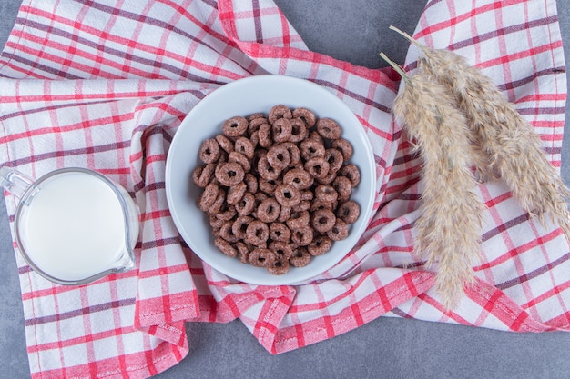 Free photo a glass of milk next to corn rings in a glass bowl next to pampas grass on the tea towel, on the marble table.