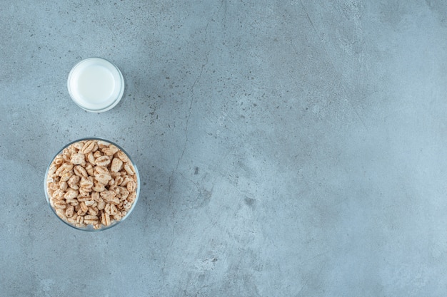 A glass of milk next to cornflakes in a glass pedestal , on the marble background.