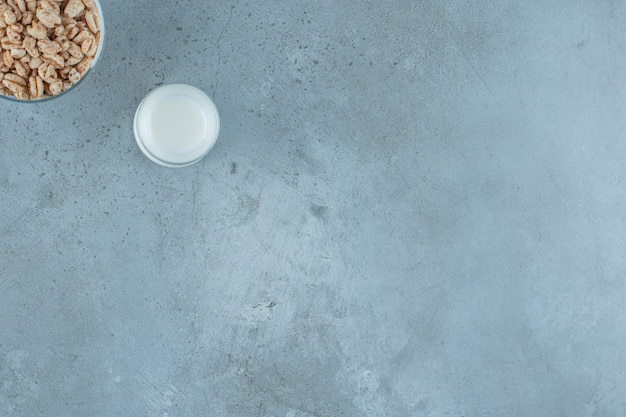 A glass of milk next to cornflakes in a glass pedestal , on the marble background.