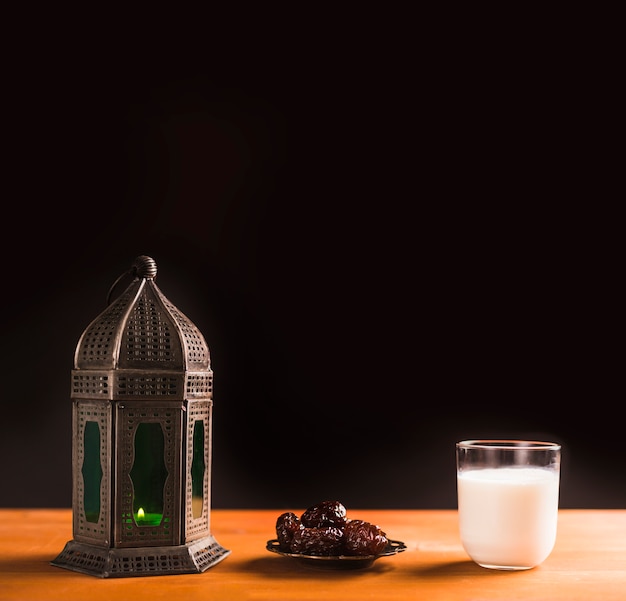 Free photo glass of milk near saucer with sweet prunes and lantern