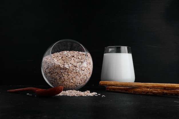 A glass of milk served with a cup of grains on black surface. 