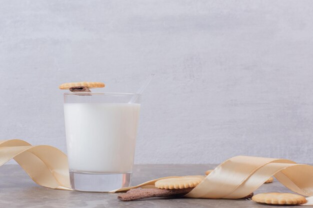 A glass of milk with cookies and band on white table.