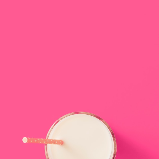 Glass of milk with drinking straw on the pink background