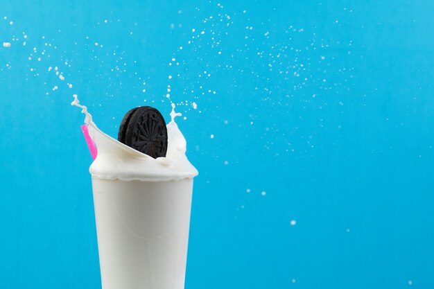 Glass of milk with a pink straw and a cookie splashing