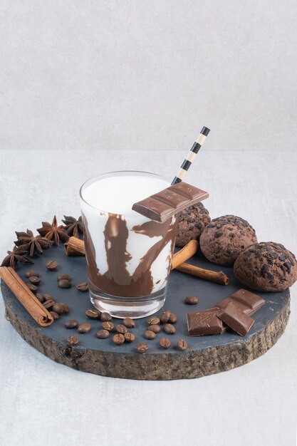 Glass of milk with straw, chocolate and cookies on wooden piece
