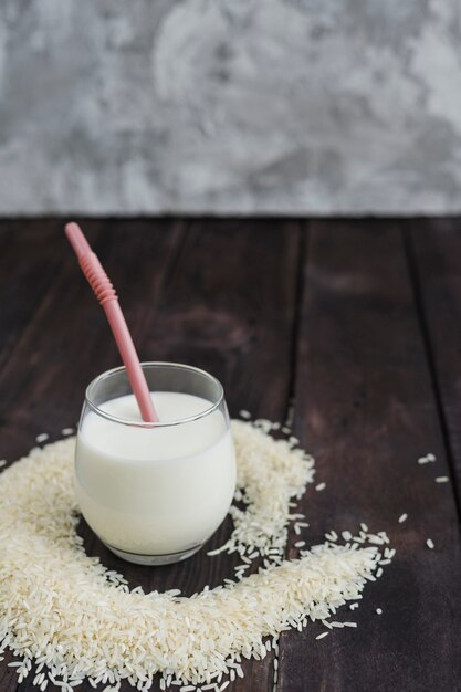 Glass of milk with straw and raw rice over wooden table