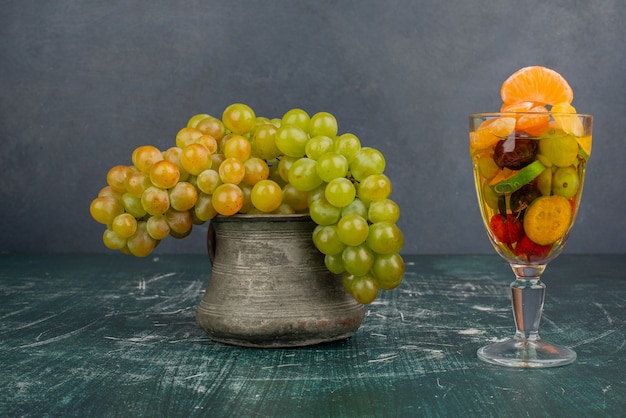 Стакан смешанных фруктов и гроздь винограда на мраморном столе.