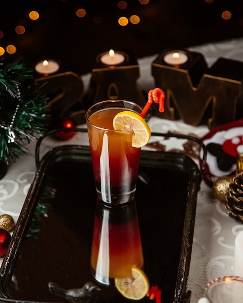 A glass of ombre cocktail garnished with lemon slice around christmas decorations