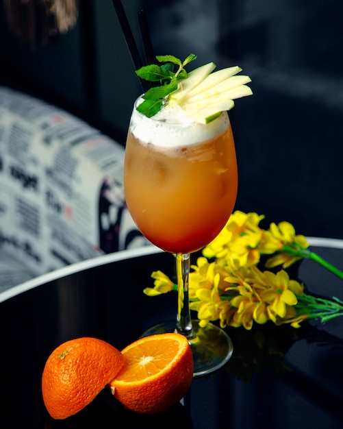 A glass of orange cocktail garnished with green apple slices