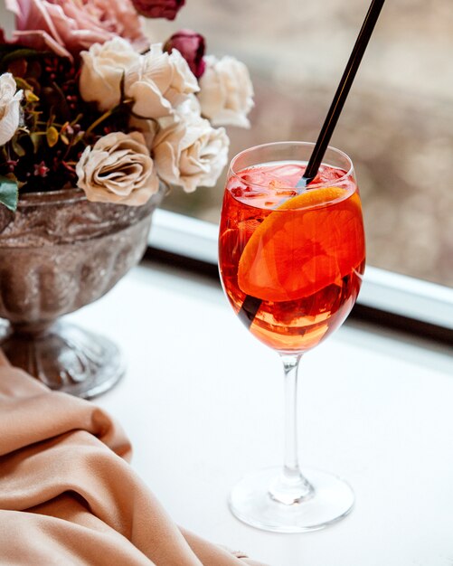 A glass of orange cocktail garnished with orange slice