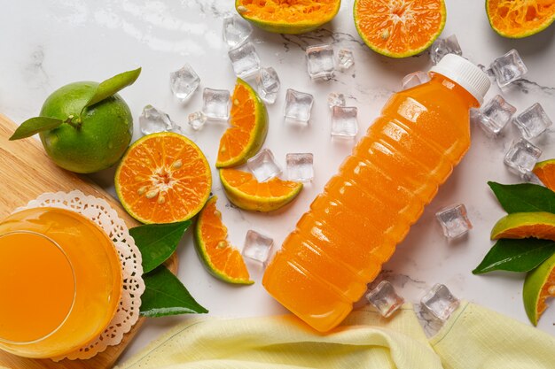 A glass of orange juice and fresh fruit on the floor with ice cubes.