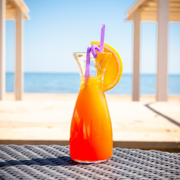 A glass of orange juice on the ground with beach. side view.