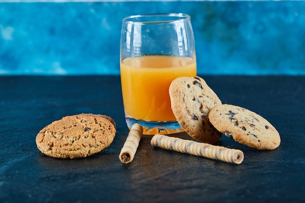 A glass of orange juice and group of various cookies on dark surface