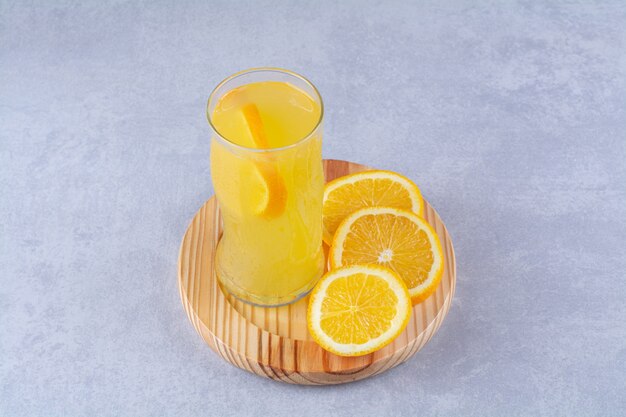 Стакан апельсинового сока рядом с ломтиком апельсина на деревянной тарелке на мраморном столе.