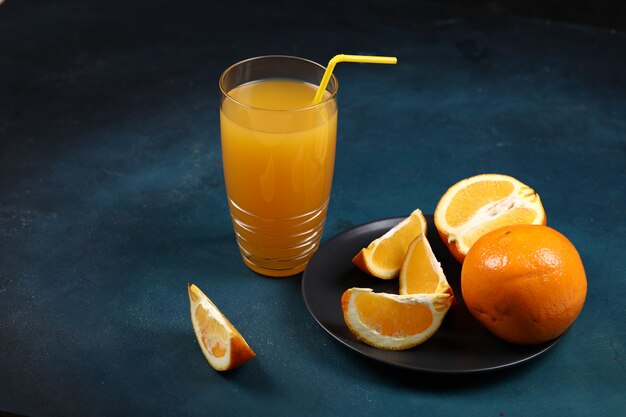 Стакан апельсинового сока с нарезанными фруктами в черной тарелке.