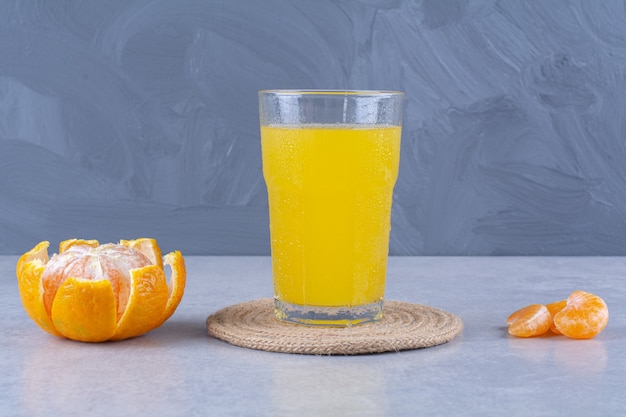 A glass of orange juicy on a trivet next to sliced tangerine on marble table.