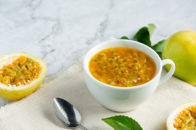 Free photo a glass of passion fruit juice and fresh passion fruit cut in half place on white fabric