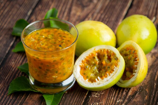 a glass of passion fruit juice and fresh passion fruit cut in half place on wooden  floor