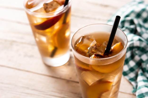 Glass of peach tea with ice cubes on wooden table