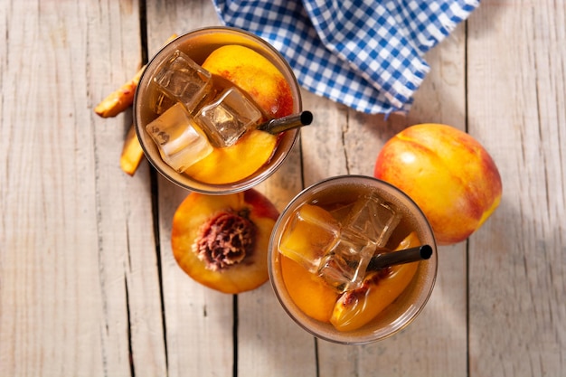 Glass of peach tea with ice cubes on wooden table