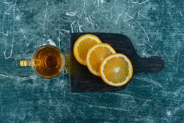 青いテーブルの上にまな板の上に梨ジュースとスライスしたオレンジのガラス。