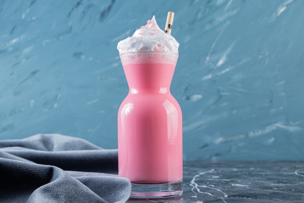 A glass pitcher of cool smoothie with whipped cream and straw.