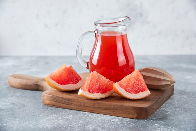 Glass pitcher of fresh grapefruit juice with slices of fruits . 