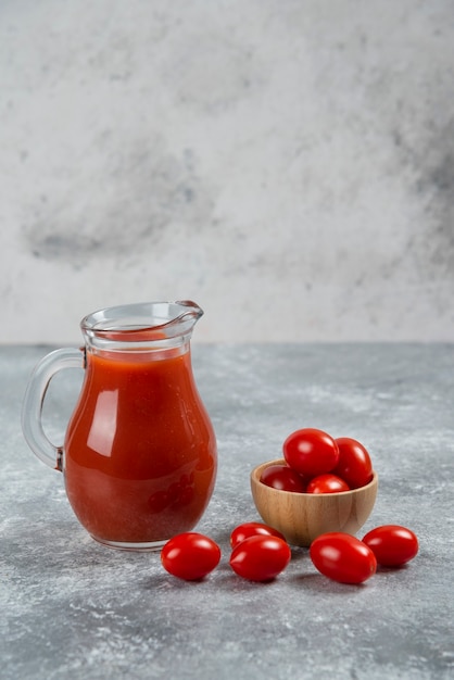 Стеклянный кувшин с томатным соком и деревянная миска с помидорами черри.