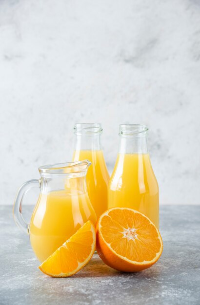 A glass pitcher of juice with fresh orange fruits on stone table .