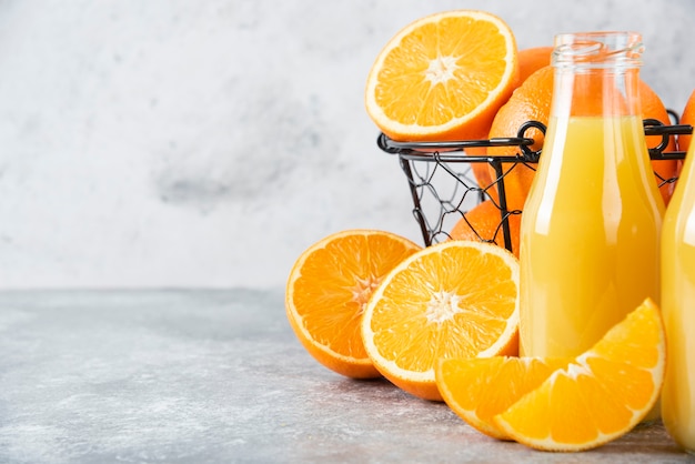 A glass pitcher of juice with fresh orange fruits on stone table .