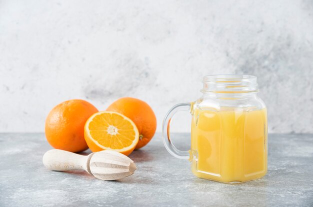 A glass pitcher of juice with fresh orange fruits on stone table .