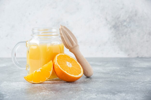 A glass pitcher of juice with fresh orange fruits on stone table .