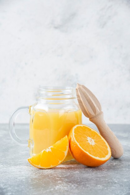 A glass pitcher of juice with fresh orange fruits on stone table .