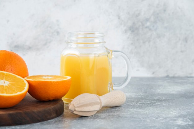 A glass pitcher of juice with fresh orange fruits on stone table .