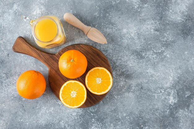 A glass pitcher of juice with fresh orange fruits on stone table .