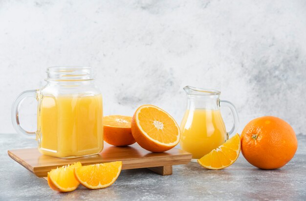 A glass pitcher of juice with fresh orange fruits on stone table .