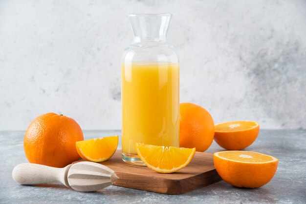 Glass pitcher of juice with fresh orange fruits on a wooden board .