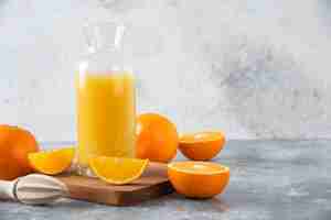 Free photo glass pitcher of juice with fresh orange fruits on a wooden board .