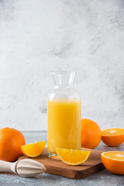 Glass pitcher of juice with fresh orange fruits on a wooden board .