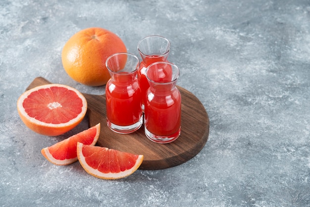 Glass pitchers of fresh grapefruit juice with slices of fruits placed on a wooden round board . 