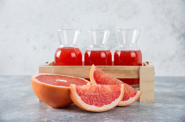 Glass pitchers of fresh grapefruit juice in wooden box with slices of fruits . 